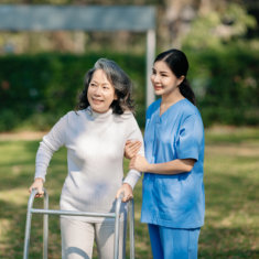 A female caregiver assisting an elderly woman walking outside